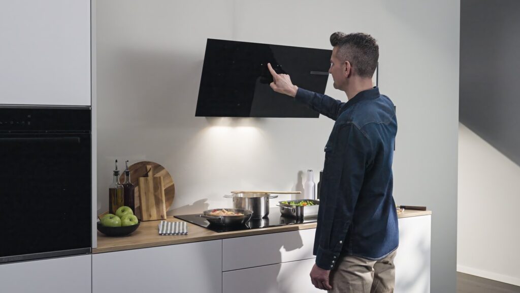 Hotte murale inclinée Bosch en verre noir allumée au-dessus d’une plaque induction, commande tactile