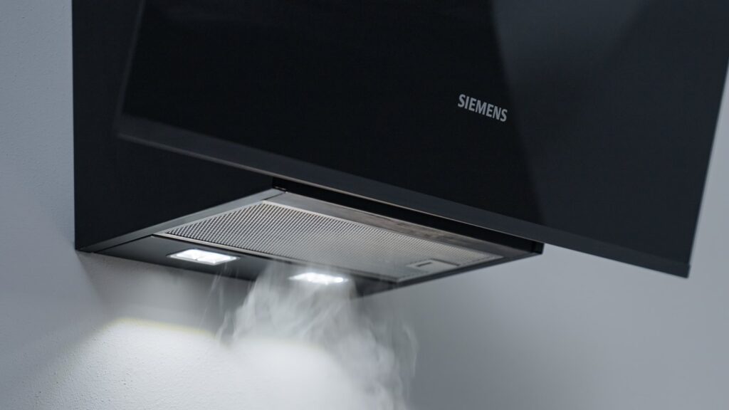 Vapeur de cuisson aspirée sous une hotte murale inclinée Siemens en verre noir, éclairage LED allumé