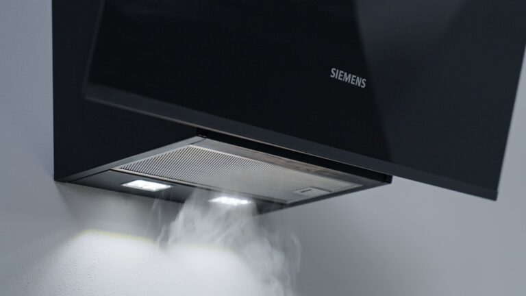 Vapeur de cuisson aspirée sous une hotte murale inclinée Siemens en verre noir, éclairage LED allumé